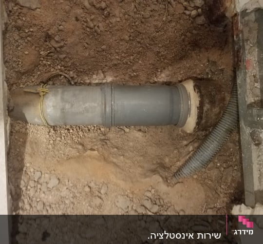צינור פלסטיק אפור מונח בתוך חפירה באדמה